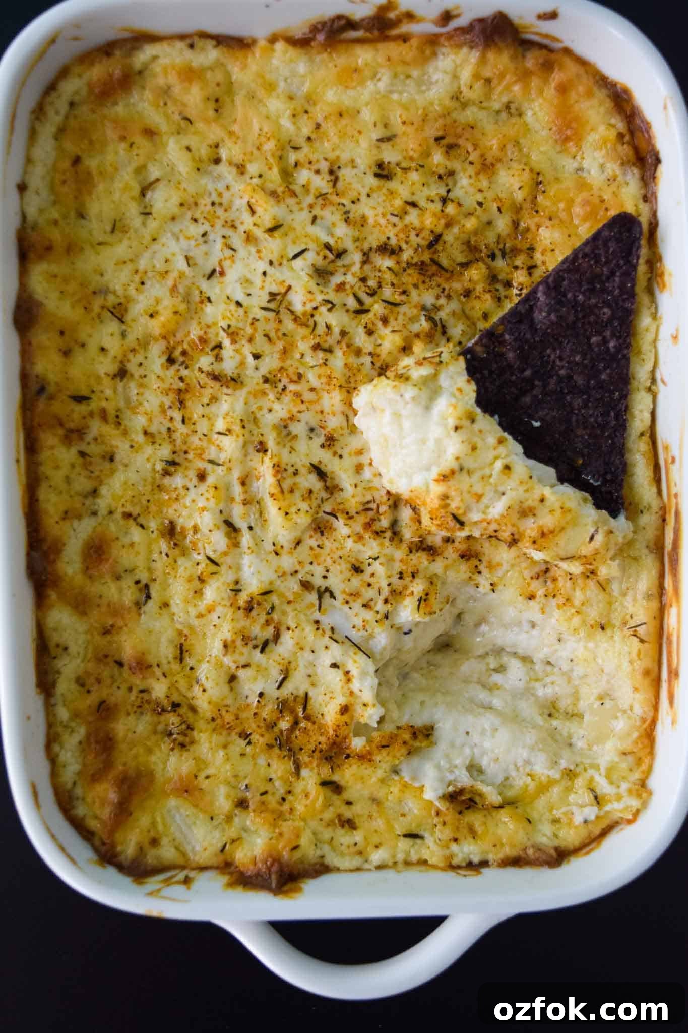 White Cheddar Onion Dip in white platter with chip dipped into it overhead shot