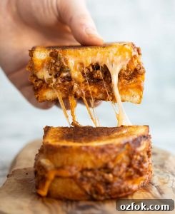 close up shot of hand lifting half of sloppy joe grilled cheese showing cheesy filling