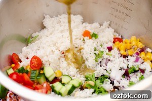 Italian style rice salad being mixed all together in a large silver bowl