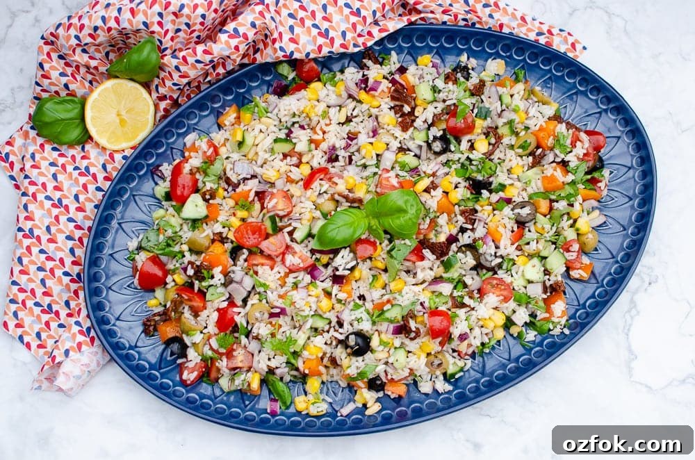 Italian Style Rice Salad on a large blue platter plate with lemon and basil on the side