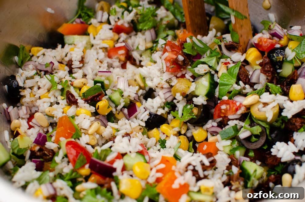 Mixing the Mediterranean salad together with wooden tongs in a silver bowl