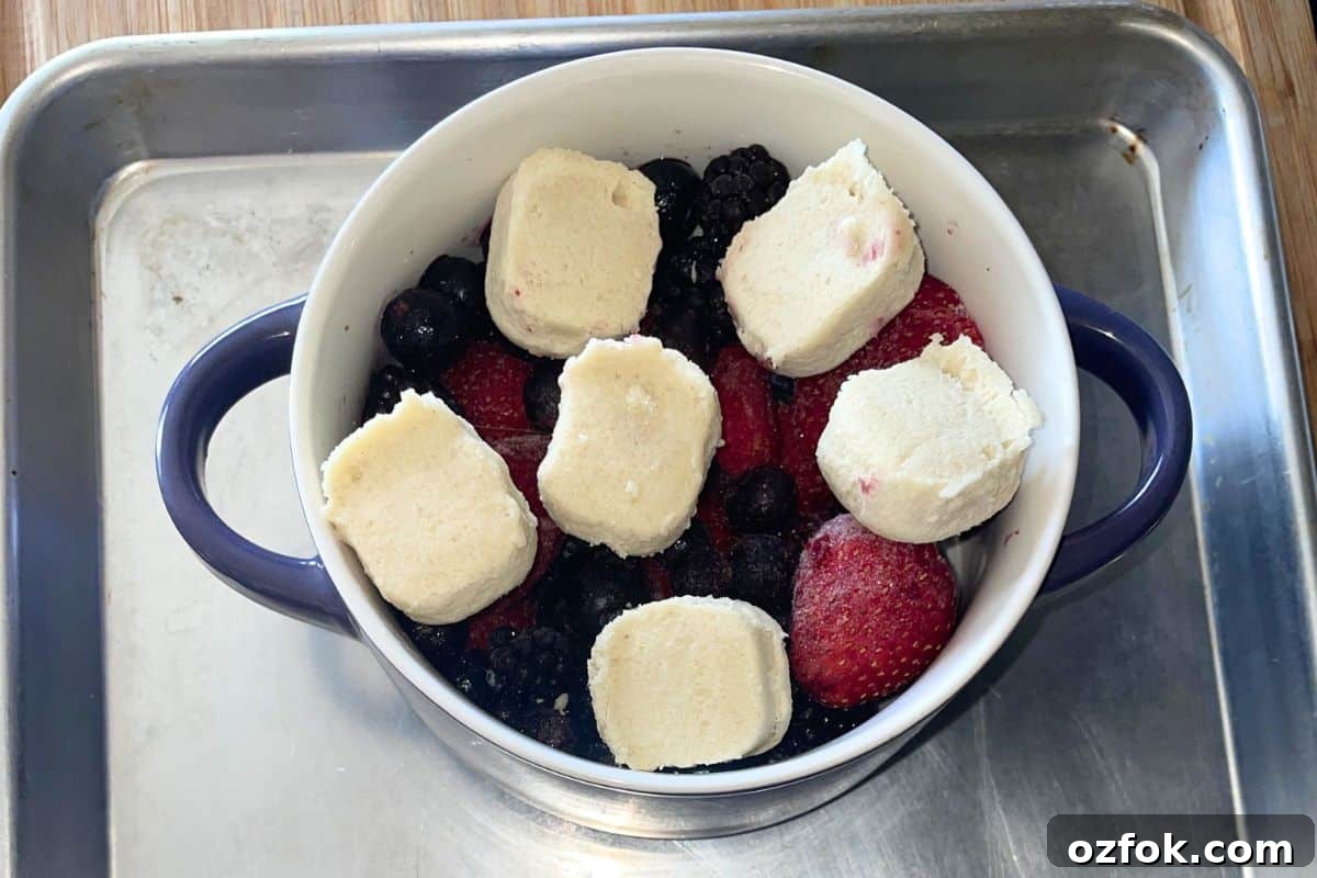 Overhead view of mixed berries topped with sliced refrigerated cookie dough in a small white baking dish, ready to go into the oven.