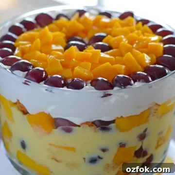 A big bowl of fruit trifle with mango pieces and grapes covering the top