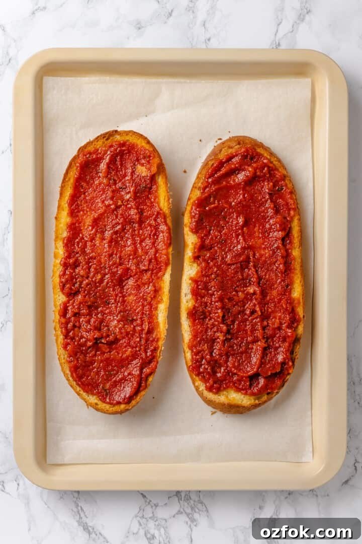 Overhead view of two French bread halves topped with pizza sauce