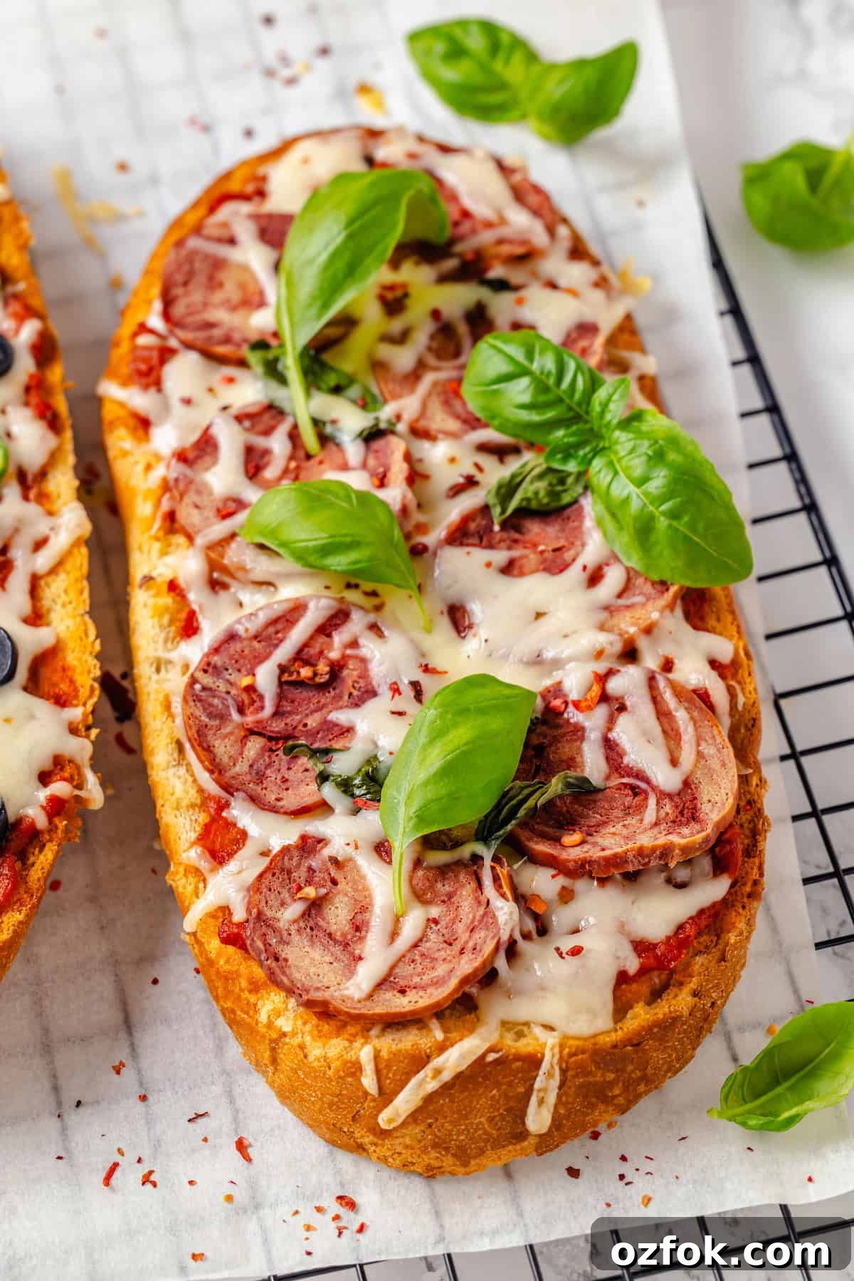 Fresh basil leaves scattered over vegan French bread pizza topped with salami