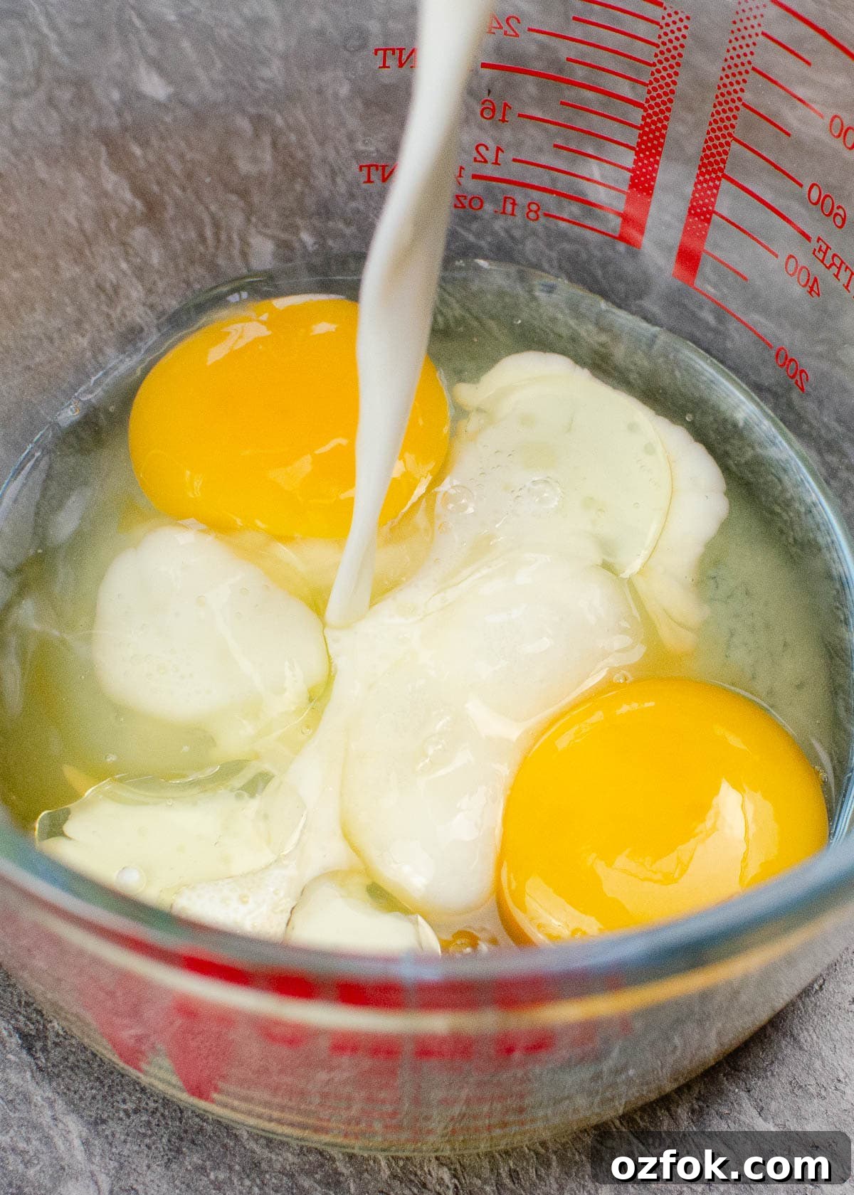 Pouring milk into a glass jug with two raw eggs to make our pancake mix