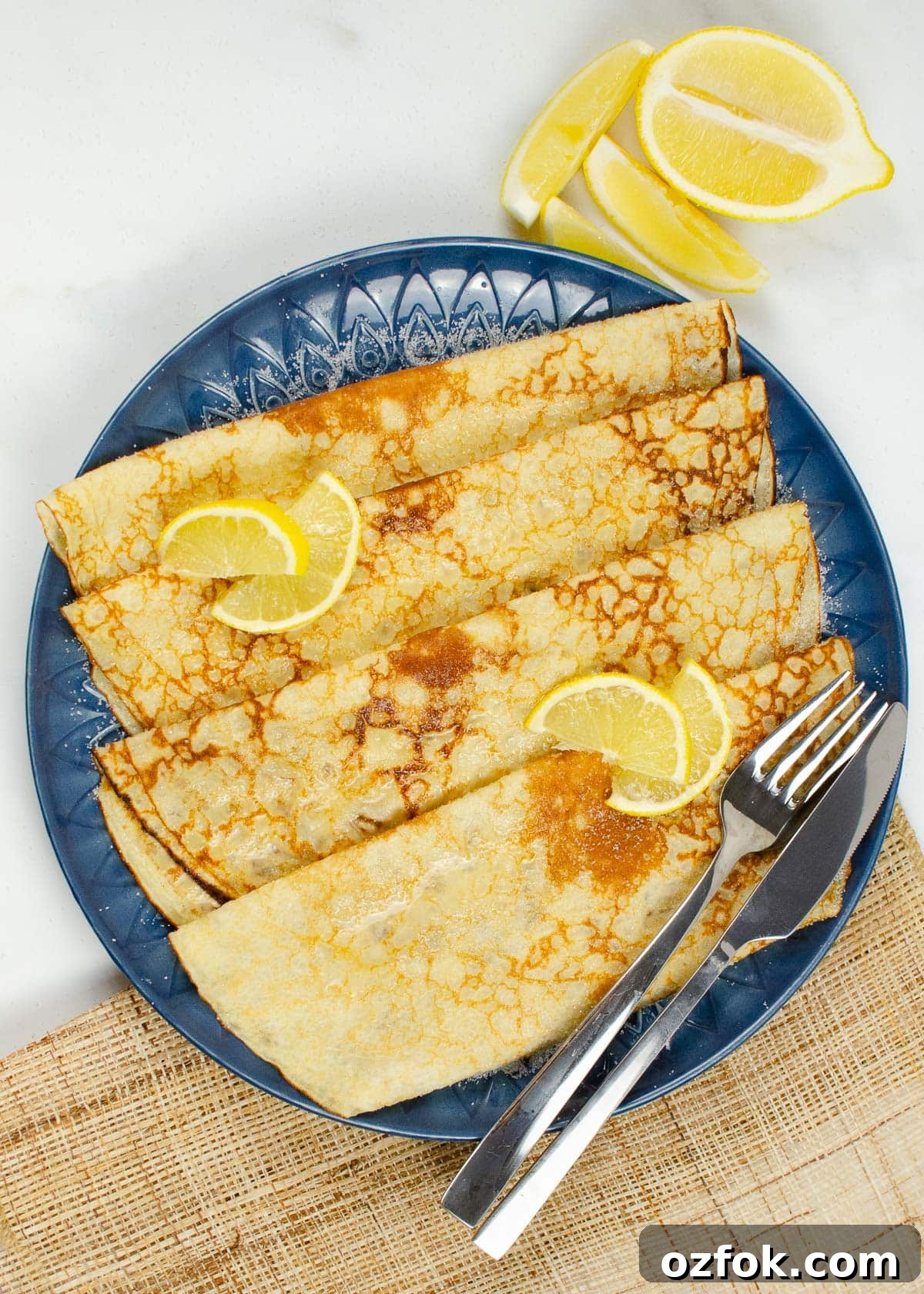Four folded Easy Homemade crepes served on a blue plate with lemon and sugar on top