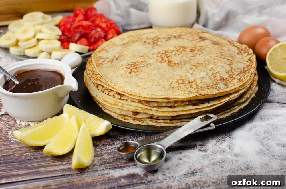 A stack of Easy English Pancakes on a black plate with toppings and ingredients around