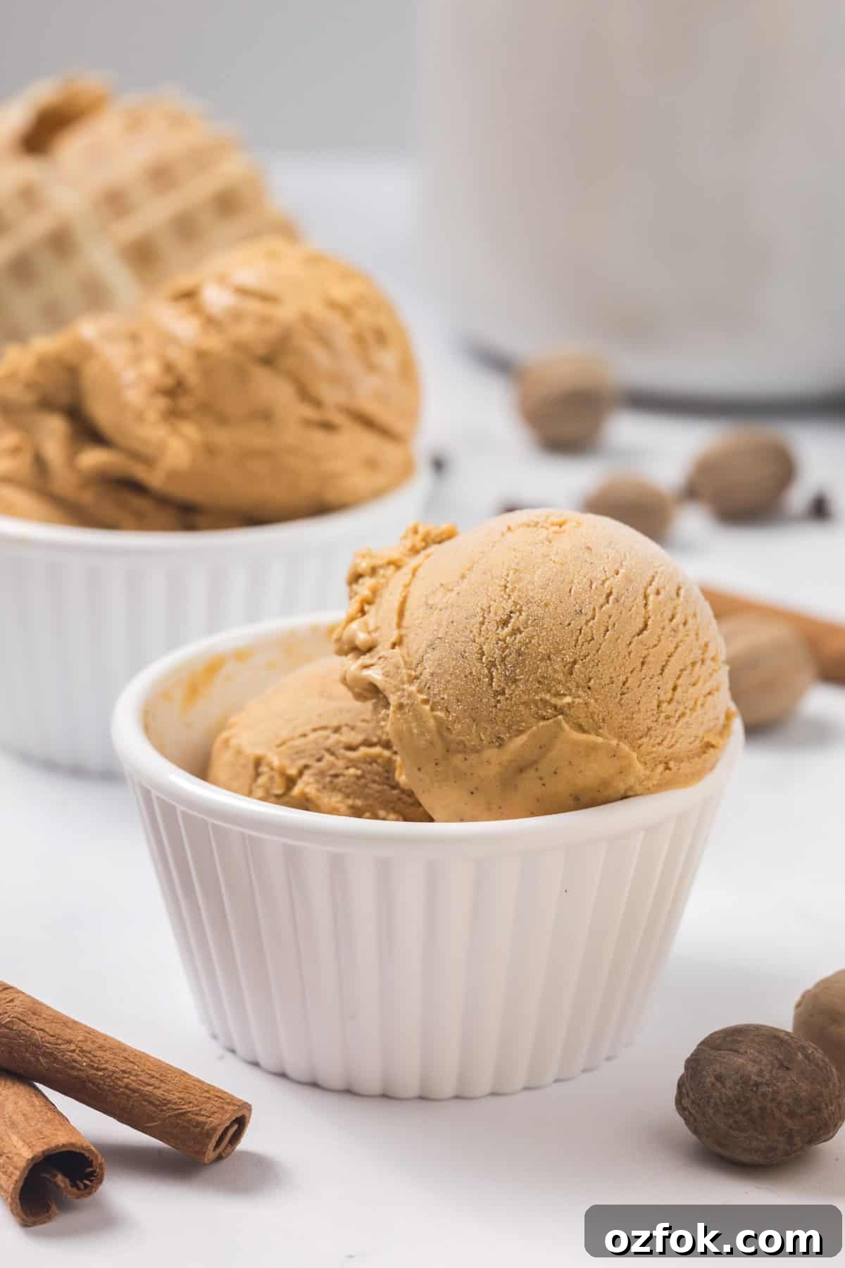 Scoops of pumpkin ice cream in a white dish. Spices and extra ice cream in the back.