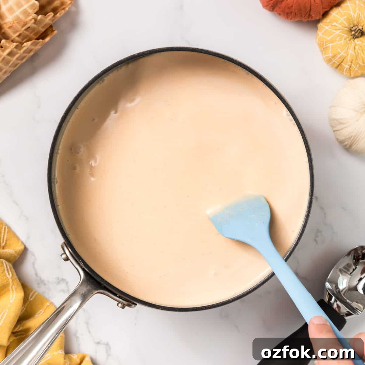 A blue spatula stirring ice cream base in a pan.