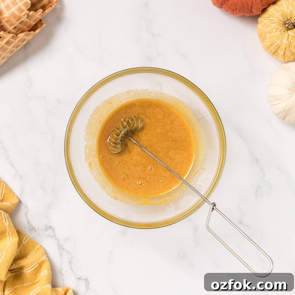 Egg yolks and a whisk inside of a clear dish.