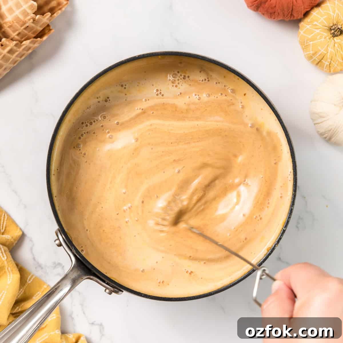 A hand whisking a creamy mixture in a pot.