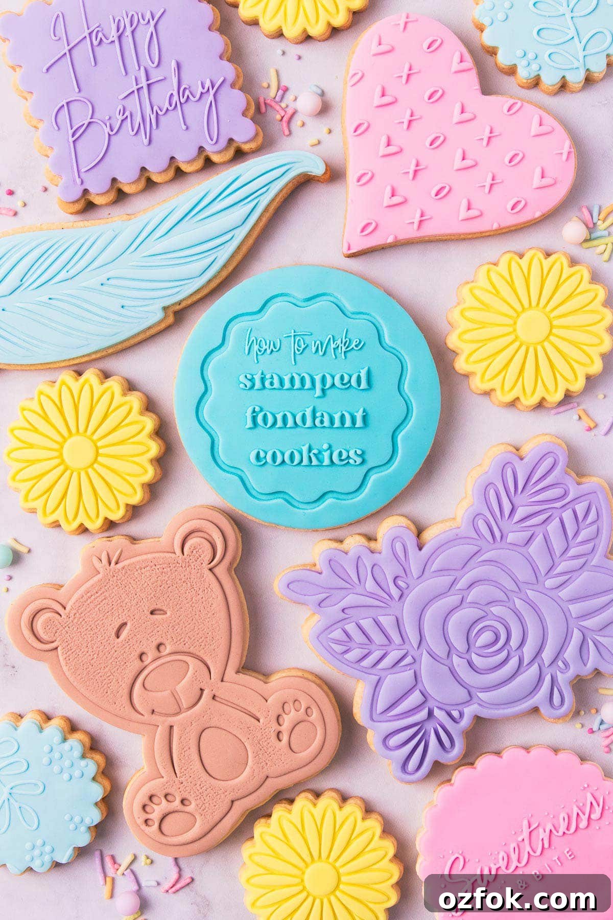 Assorted stamped fondant cookies on a grey background, the middle cookie has a stamped design saying "how to make stamped fondant cookies".
