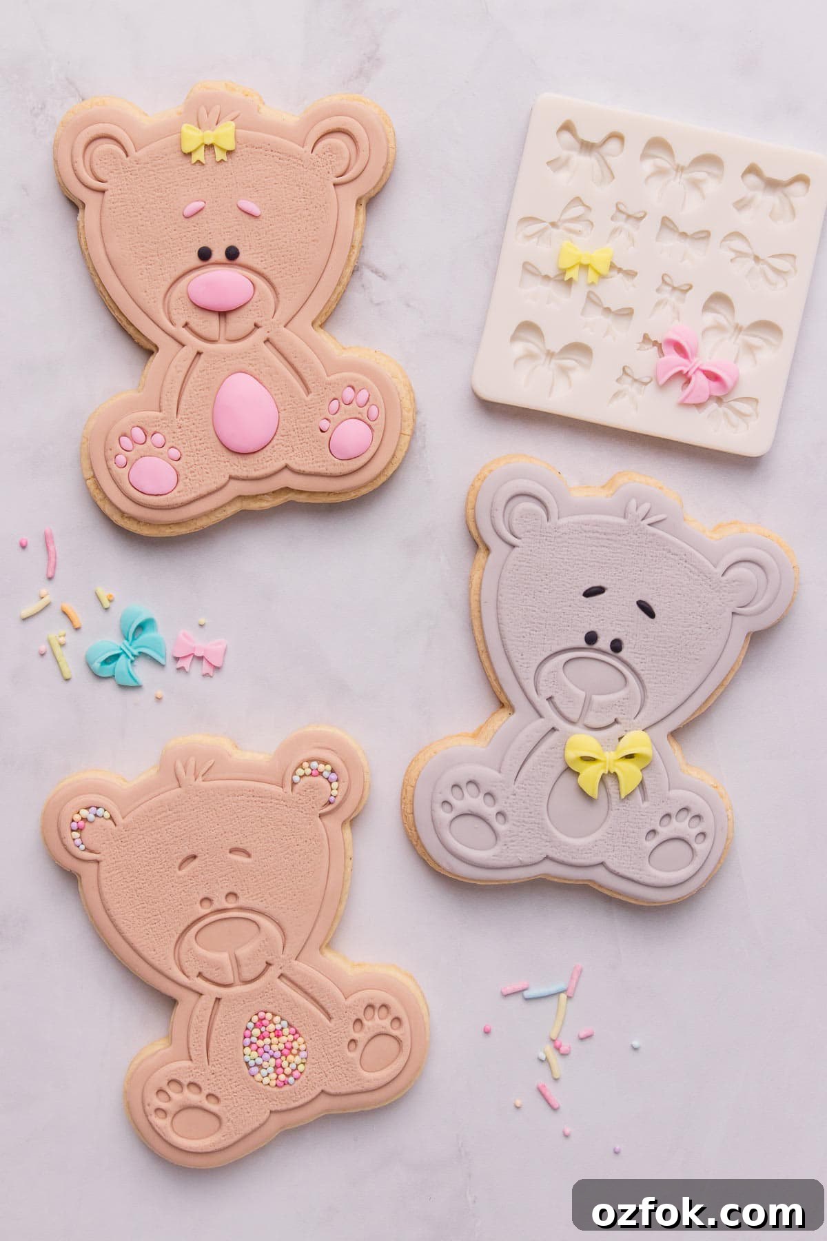 Three cute teddy bear shaped stamped fondant cookies, one bear is grey and the other two are light brown, and they're decorated with little bows and sprinkles.